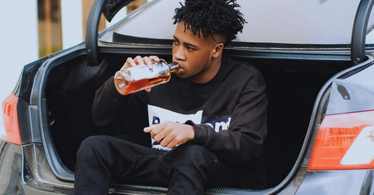 Man sitting in a car trunk drinking alcohol